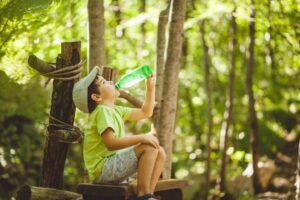 Boy Resting On Bench under the tree Drinking Water From Bottle